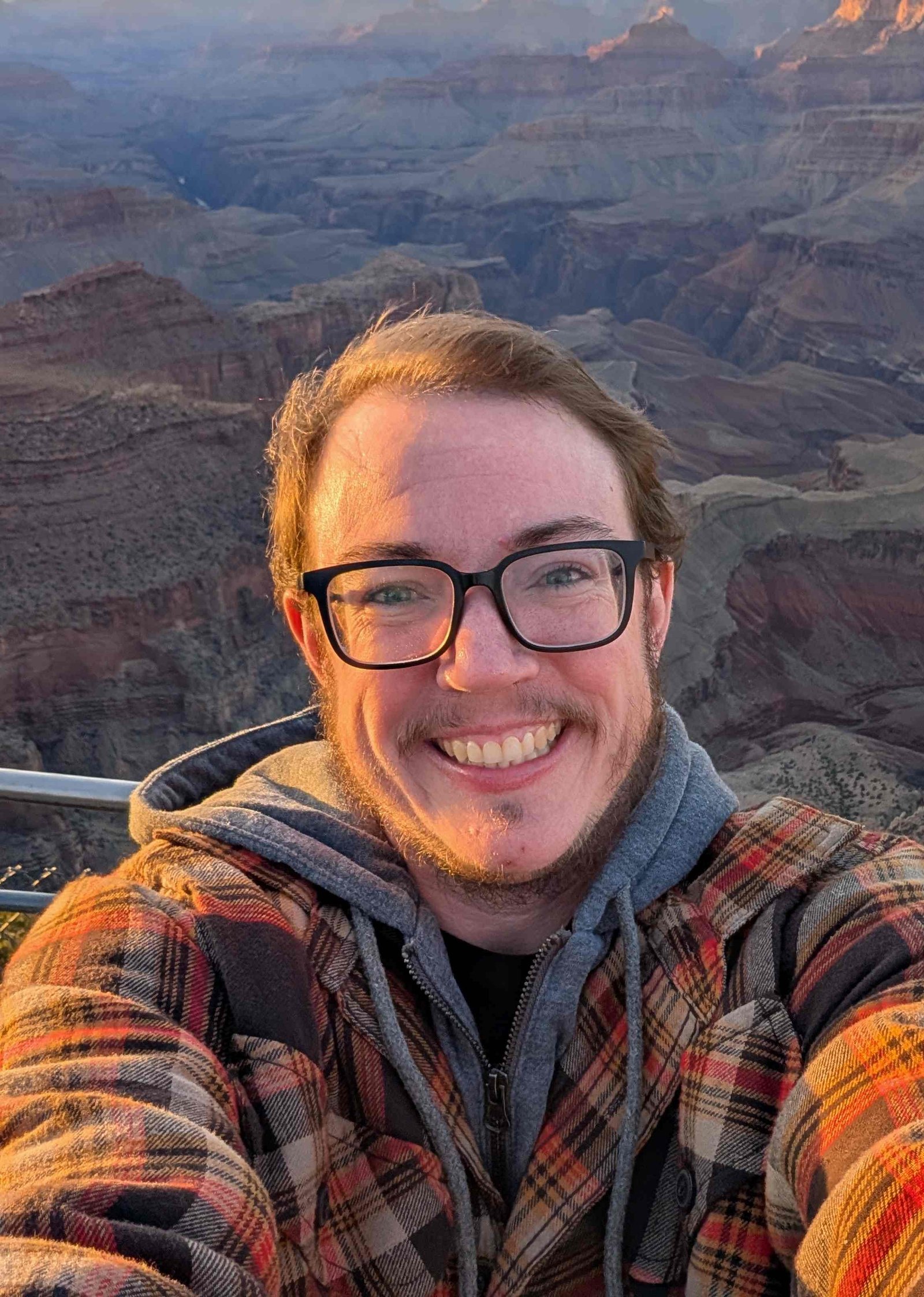 Simon, a white man with brown hair and glasses standing in front of the grand canyon at sunset